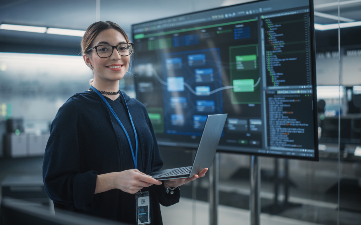 AI Implementation - Woman with laptop standing in front of large computer monitor