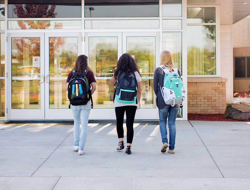 Three students walking towards campus building entrance