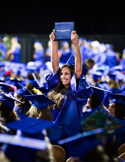 Graduate holding degree up above crowd